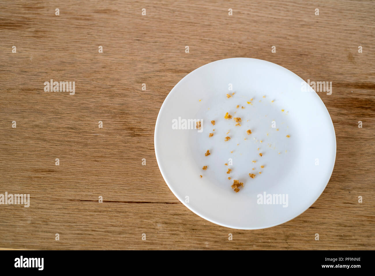 White Plate with Food Crumbs Only Sitting on a Wood Table - All Finished Stock Photo