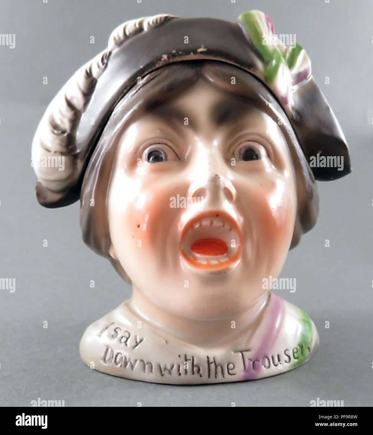 Ceramic tobacco jar, with a removable hat, depicting a suffragette wearing the purple, green, and white colors of the militant Women's Political and Social Union, with an open mouth and an angry look on her face, and a caption on the base reading 'down with the trousers', 1900. () Stock Photo