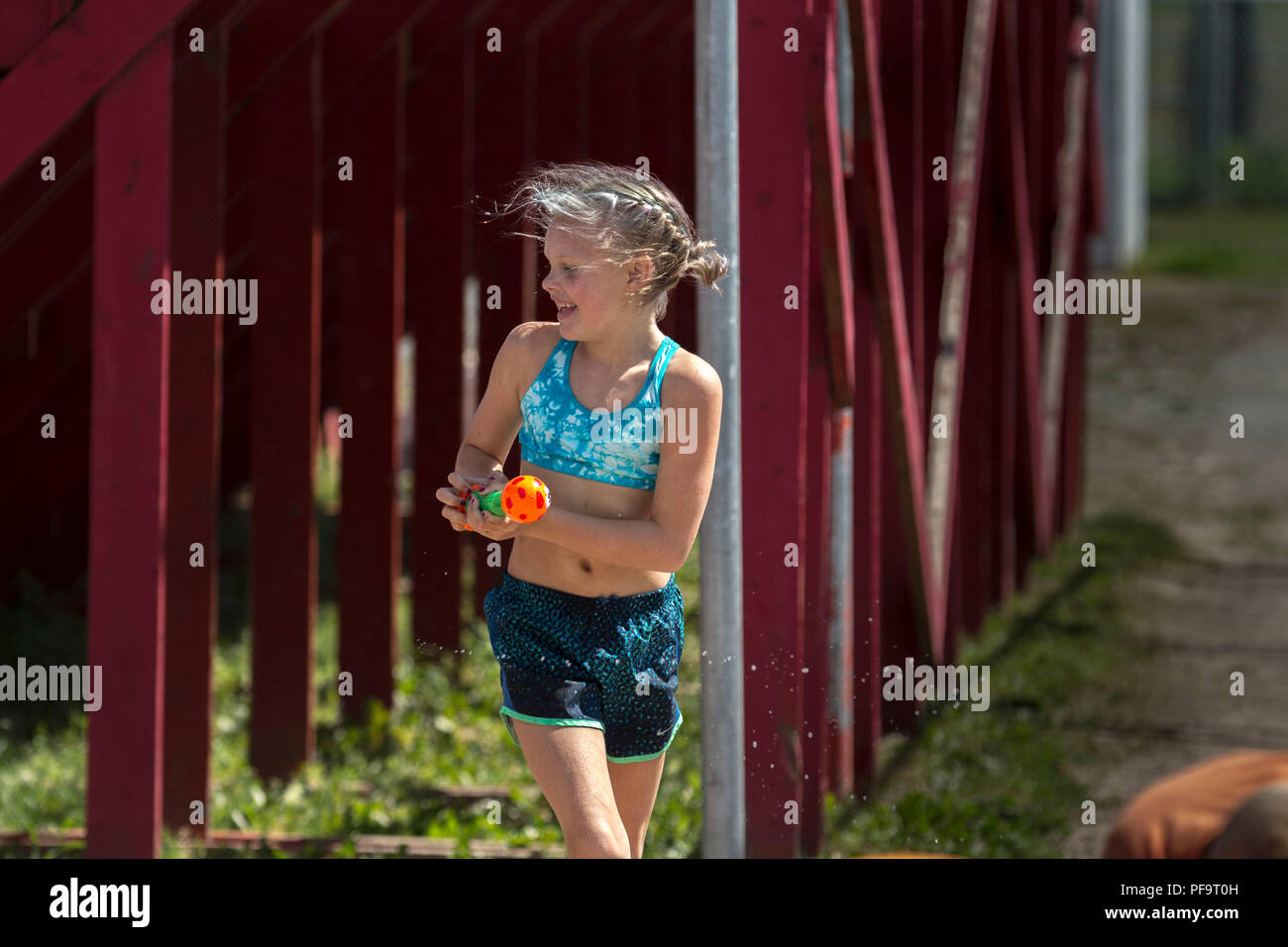Summer time fun, kids and adults using pails, squirt guns and soakers, in a water fight. Smiling blonde with water gun, laughing. Model Released, Stock Photo