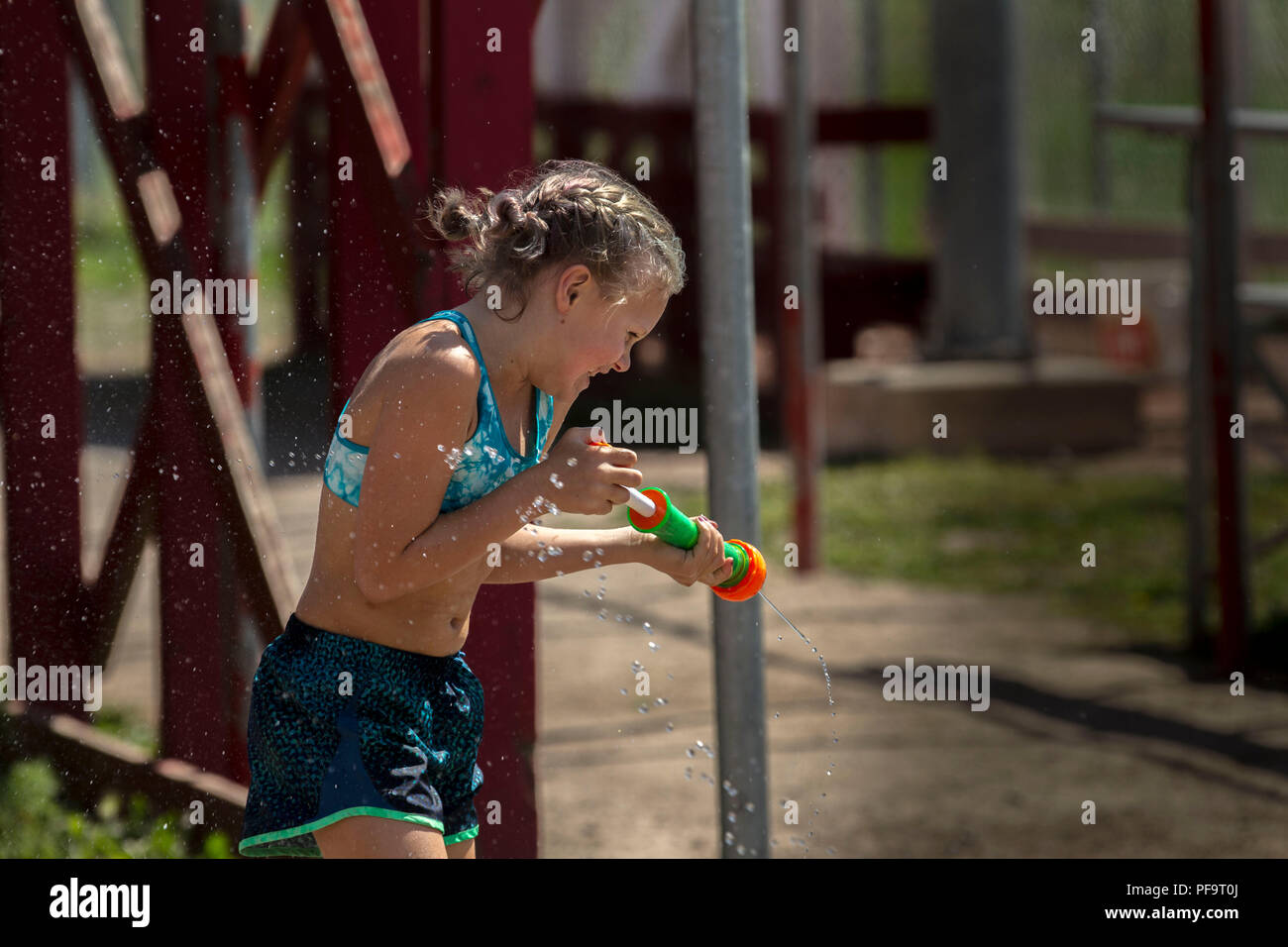 Summer time fun, kids and adults using pails, squirt guns and soakers, in a water fight. Smiling blonde with water gun, laughing. Model Released. Stock Photo