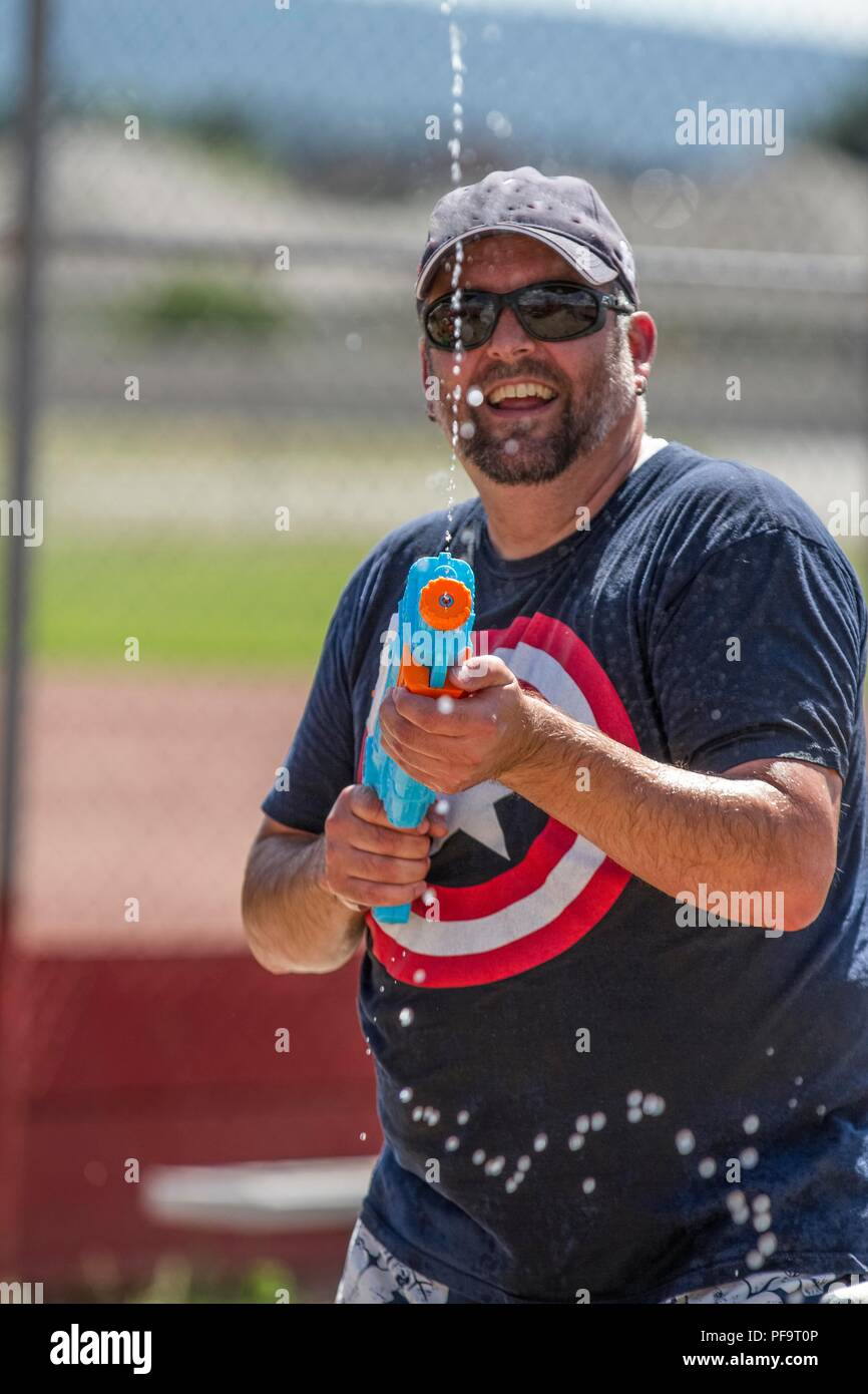 Summer time fun, kids and adults using pails, squirt guns, in a water fight. Smiing adult man, firing a burst of water and laughing. Model Released. Stock Photo