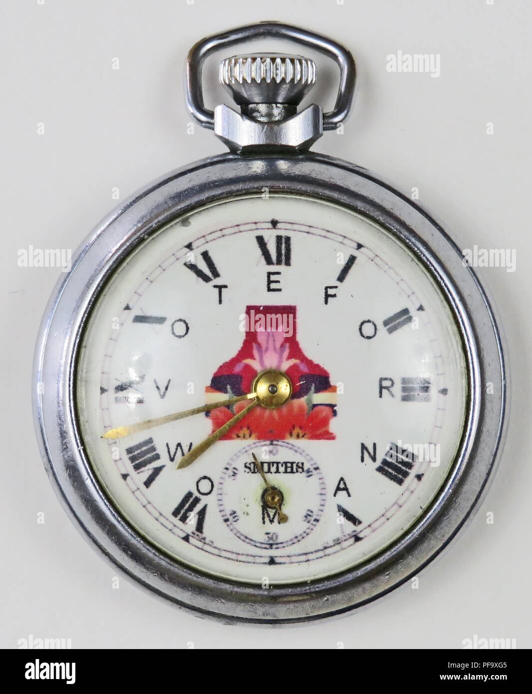 Silver-colored, pro-suffrage pocket watch or fob watch, with the phrase 'Vote for Woman,  with each letter corresponding to a Roman numeral, and a red floral design in the center of the enamel face, labeled 'Smiths', 1900. Photography by Emilia van Beugen. () Stock Photo