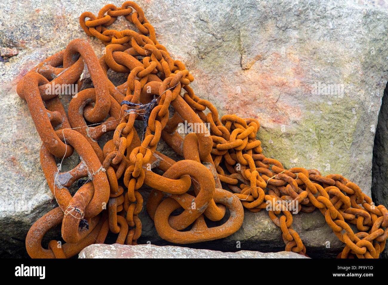 Rusty iron chains in a heap on rocks shot from above Stock Photo