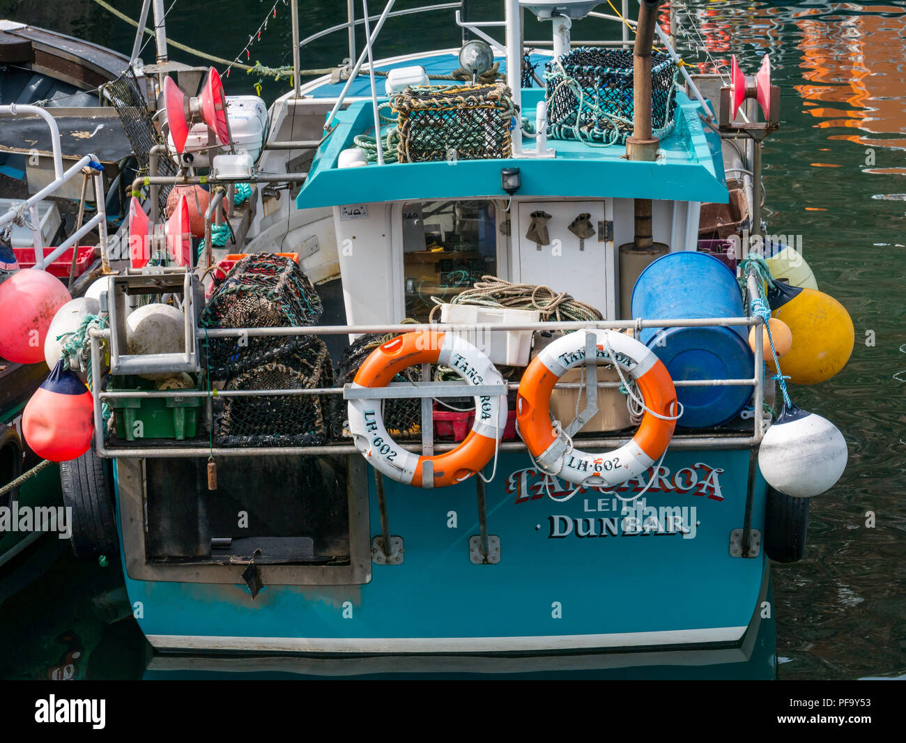 Close up of fishing boat with lobster pots or creels, lifebelts and bumpers in harbour, Dunbar, East Lothian, Scotland, UK Stock Photo