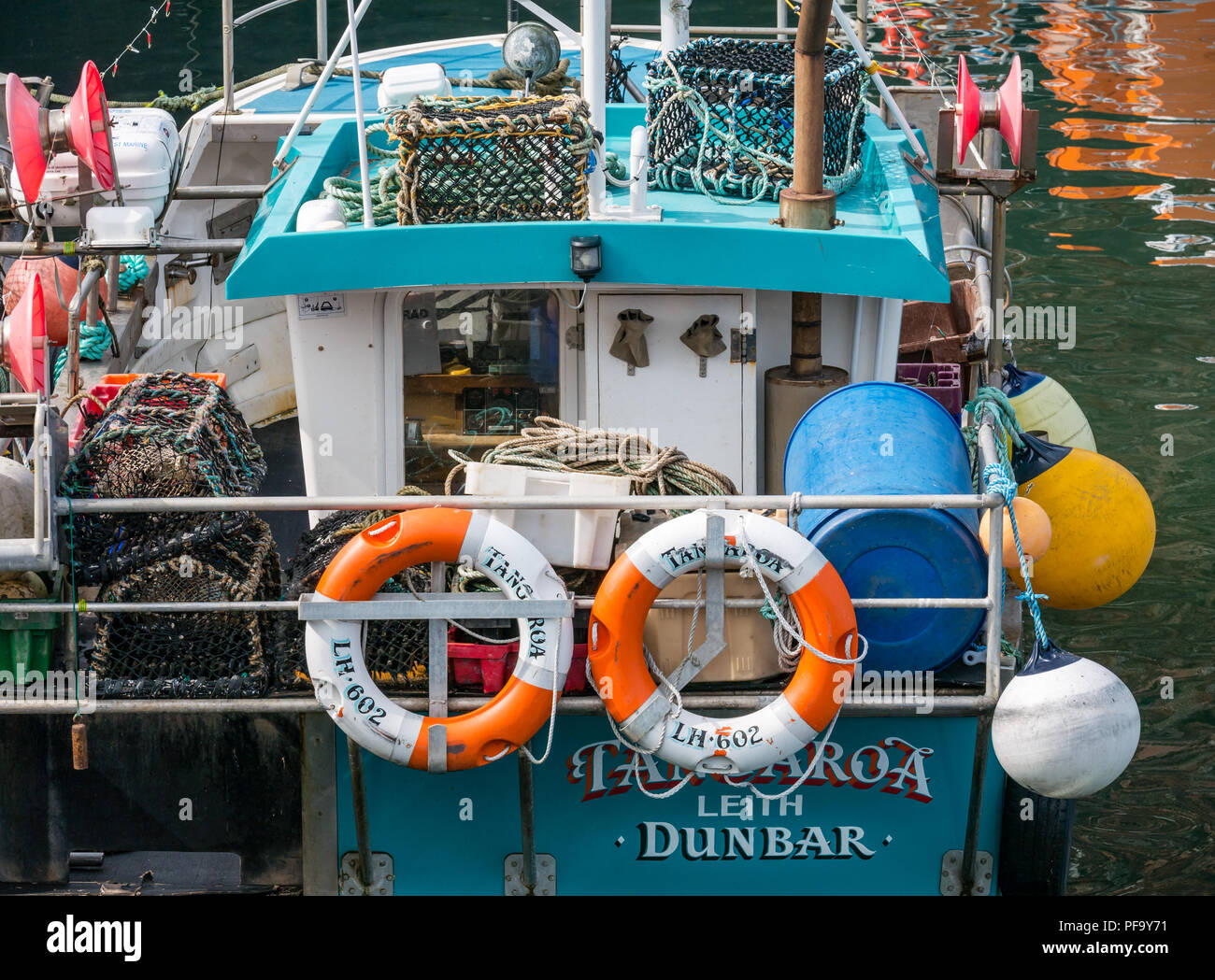 Close up of fishing boat with lobster pots or creels, lifebelts and bumpers in harbour, Dunbar, East Lothian, Scotland, UK Stock Photo