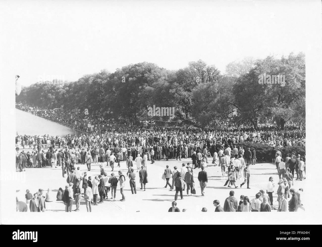 Black and white photograph, showing a crowd of people standing and walking on a paved area of the National Mall surrounding the Lincoln Memorial Reflecting Pool, during a march to protest the Vietnam War, photographed in Washington DC, United States, 1969. () Stock Photo