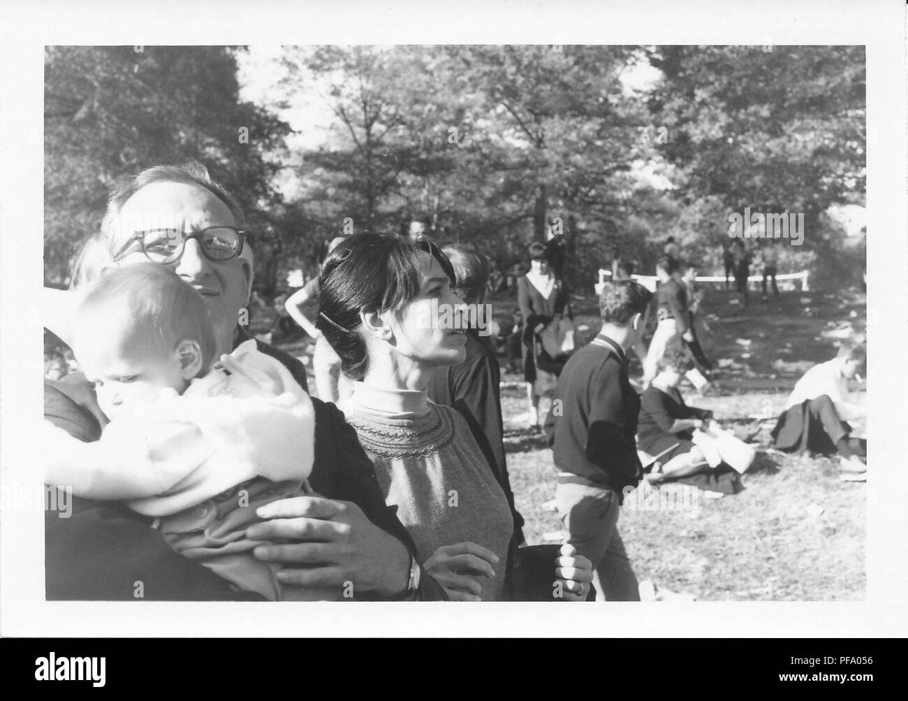 Black and white photograph, depicting a man wearing glasses and holding a baby in the foreground, with a woman in profile, standing just behind him, and several more people in the background, gathered outdoors to protest the Vietnam War, in Washington DC, United States, 1969. () Stock Photo