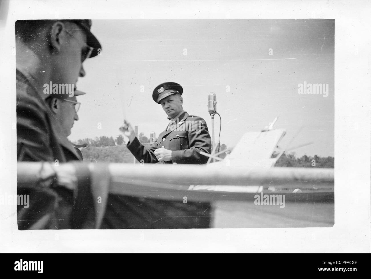 Black and white photograph, showing a conductor, wearing military clothes (with wings on his sleeve suggesting US Air Force affiliation) standing next to a microphone, in front of two musicians who are looking toward a music stand, likely photographed in Ohio, during the Seventh War Loan drive, near the end of World War II, 1945. () Stock Photo