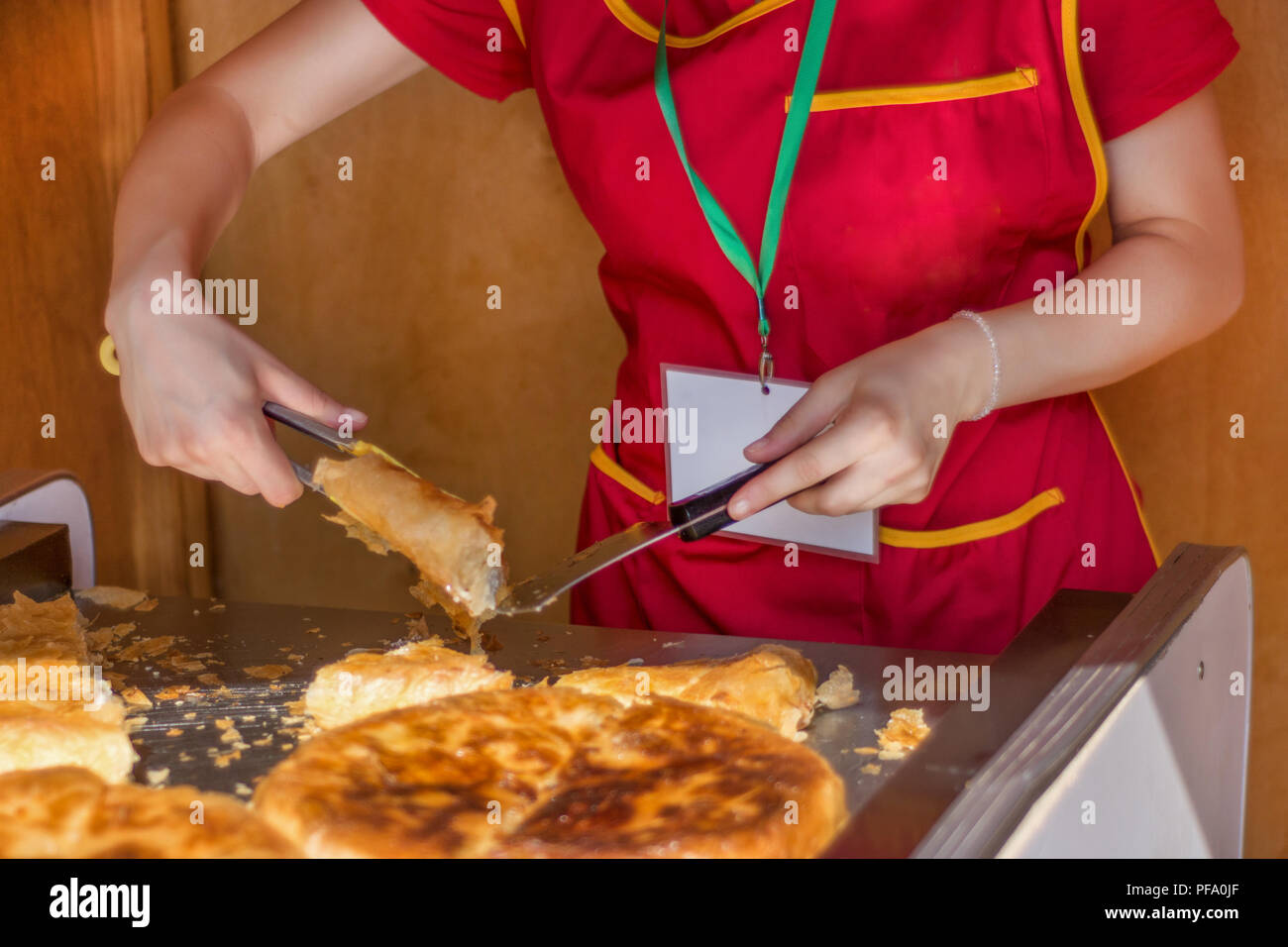 Young girl worker cuts a Balkan burek with cheese in bakery shop. Traditional pie breakfast in the Balkans concept. Close up, selective focus Stock Photo