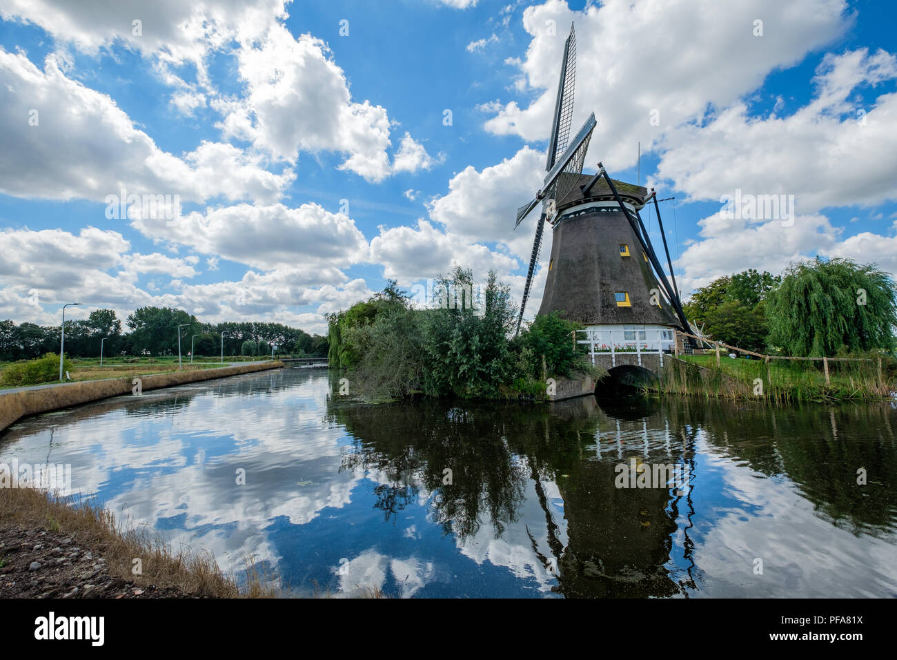Dutch windmill reflected in the water and cloudy blue sky. Stock Photo