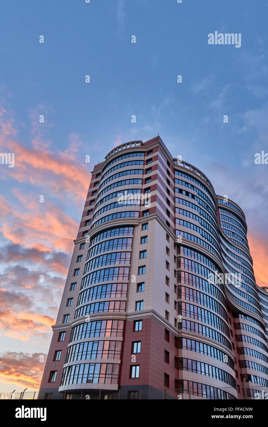 Tall modern skyscraper with a unique shape surrounded by pink clouds shot on the sunset, copy space above Stock Photo