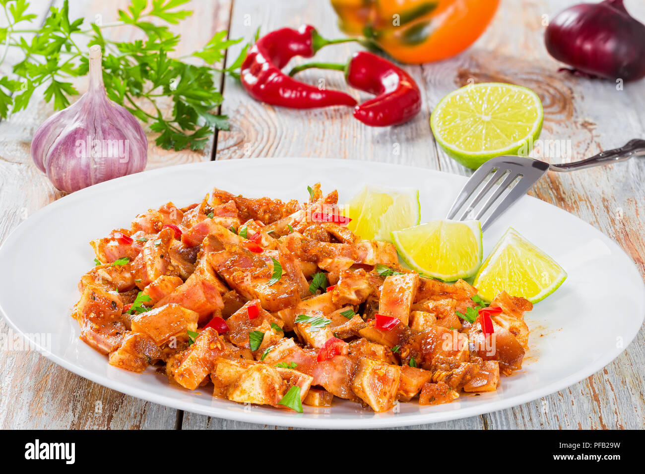 Sliced Pig Ears or Oreja de Cerdo marinated with spices,  bell pepper and vinegar on white platter with fork,  garlic parsley, chilli, bell pepper on  Stock Photo