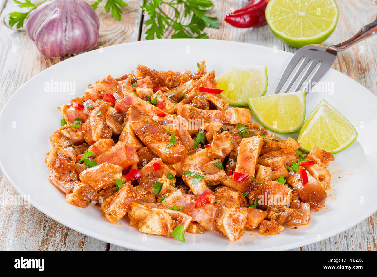 Braised Pig Ears or Oreja de Cerdo with spices, chili pepper, pieces of lime sprinkled with parsley on white platter on natural wooden old boards, clo Stock Photo