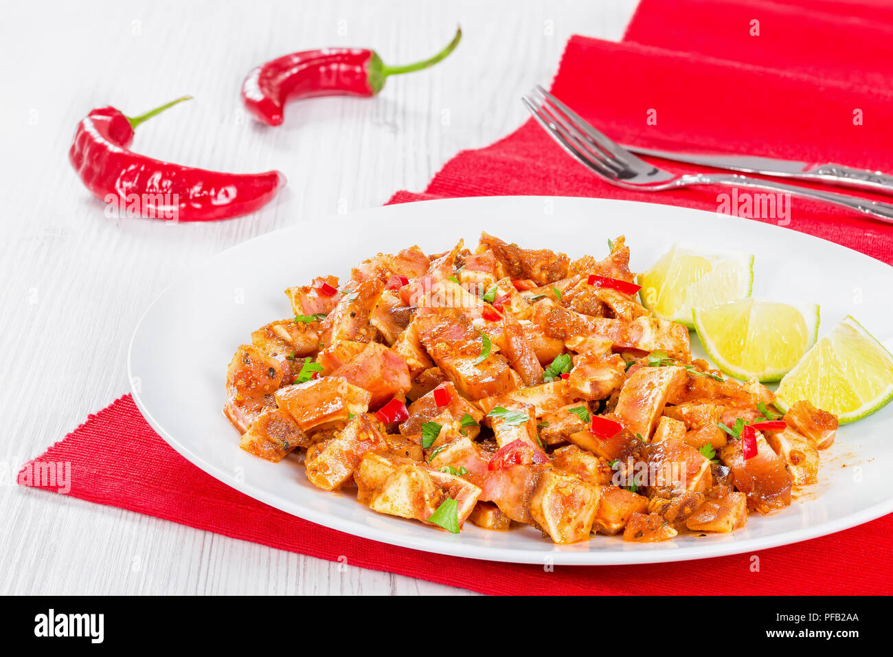 cooked and marinated Pig Ears or Oreja de Cerdo with spices, chili pepper, pieces of lime sprinkled with parsley on white platter on wooden old boards Stock Photo