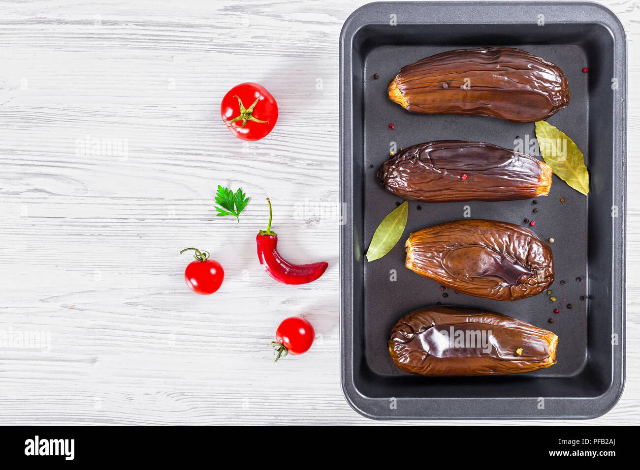 oven baked eggplants in baking dish with bay leaves and spices on white table, view from above