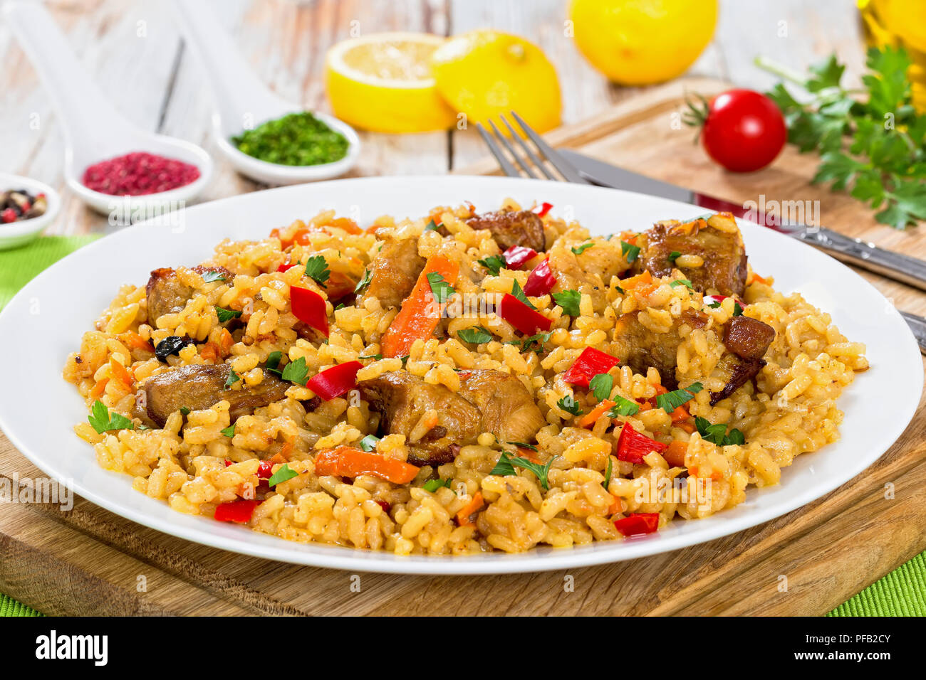 paella with meat, pepper, vegetables and spices on dish on cutting board, lemon slice, spices and cherry tomatoes on background, view from above, clos Stock Photo