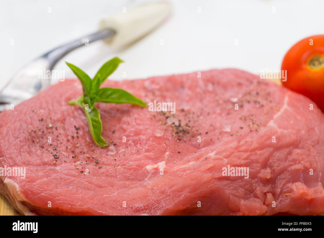 raw beef steak on cutting board with cherry tomatoes and basil leaf
