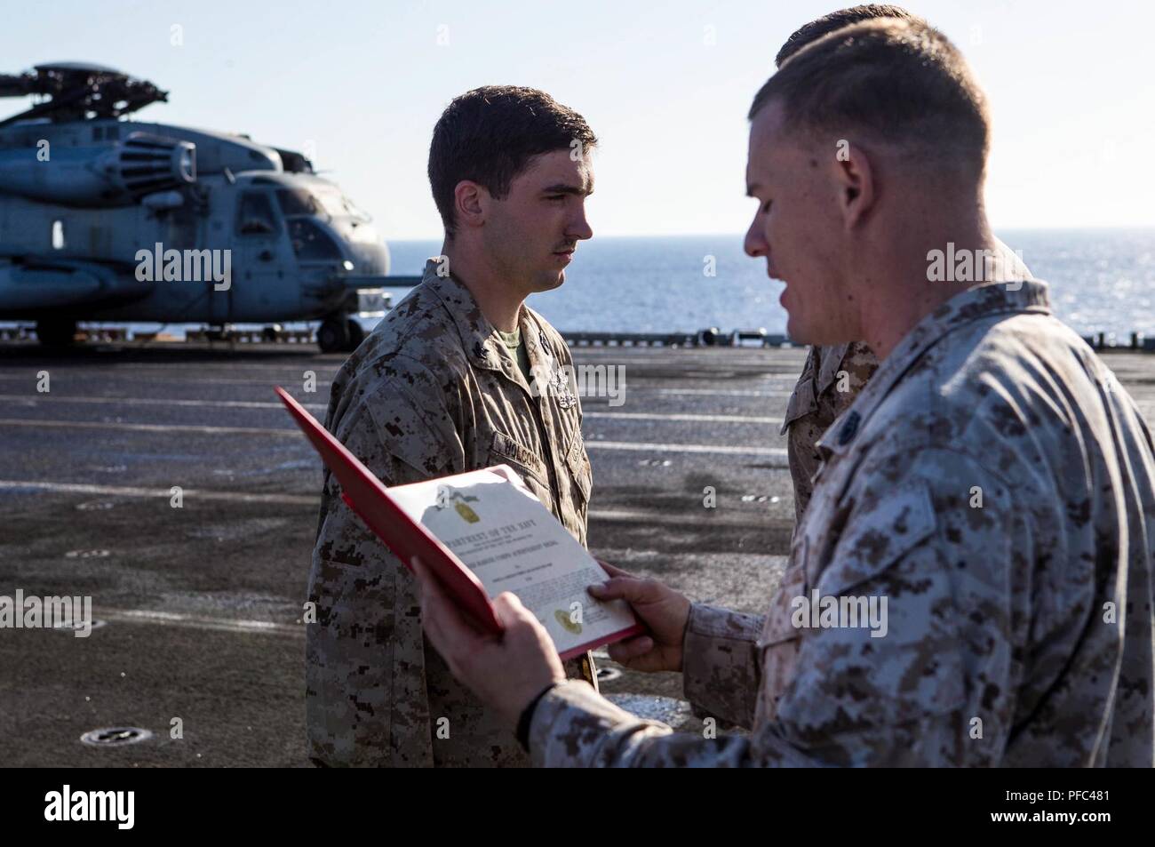 U.S. 5TH FLEET AREA OF OPERATIONS (June 5, 2018) U.S. Navy Hospital Corpsman Petty Officer Third Class Jacob M. Holcomb, left, assigned to Battalion Landing Team, 2nd Battalion, 6th Marine Regiment (BLT 2/6), 26th Marine Expeditionary Unit (MEU), stands at attention during the reading of his Navy Achievement Medal (NAM) citation aboard the Wasp-class amphibious assault ship USS Iwo Jima (LHD 7), June 5, 2018. Iwo Jima and the 26th MEU are conducting naval operations in the U.S. 5th Fleet area of operations. Stock Photo