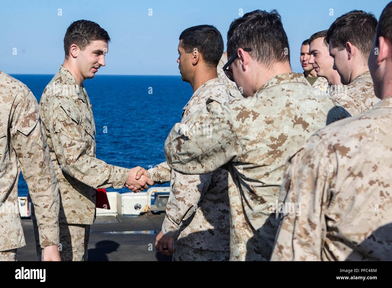 U.S. 5TH FLEET AREA OF OPERATIONS (June 5, 2018) U.S. Navy Hospital Corpsman Petty Officer Third Class Jacob M. Holcomb, left, assigned to Battalion Landing Team, 2nd Battalion, 6th Marine Regiment (BLT 2/6), 26th Marine Expeditionary Unit (MEU), shakes hands with Marines after receiving a Navy Achievement Medal (NAM) aboard the Wasp-class amphibious assault ship USS Iwo Jima (LHD 7), June 5, 2018. Iwo Jima and the 26th MEU are conducting naval operations in the U.S. 5th Fleet area of operations. Stock Photo