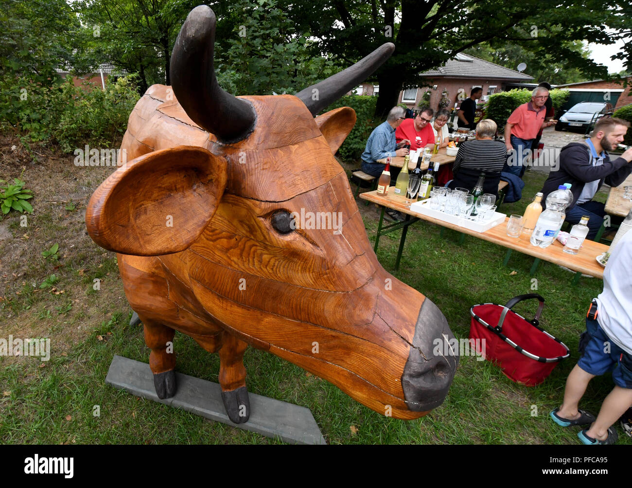 Aukrug-Homfeld, Germany. 19th Aug, 2018. The wooden cow 'Gerda Muh' stands in front of visitors of a neighbourhood meeting. An anonymous artist created the wooden cow, since Whitsun it has appeared in changing gardens in the district of Homfeld. With this event, the initiator wants to stimulate the discussion about agriculture and the community feeling of the villagers. Credit: Carsten Rehder/dpa/Alamy Live News Stock Photo