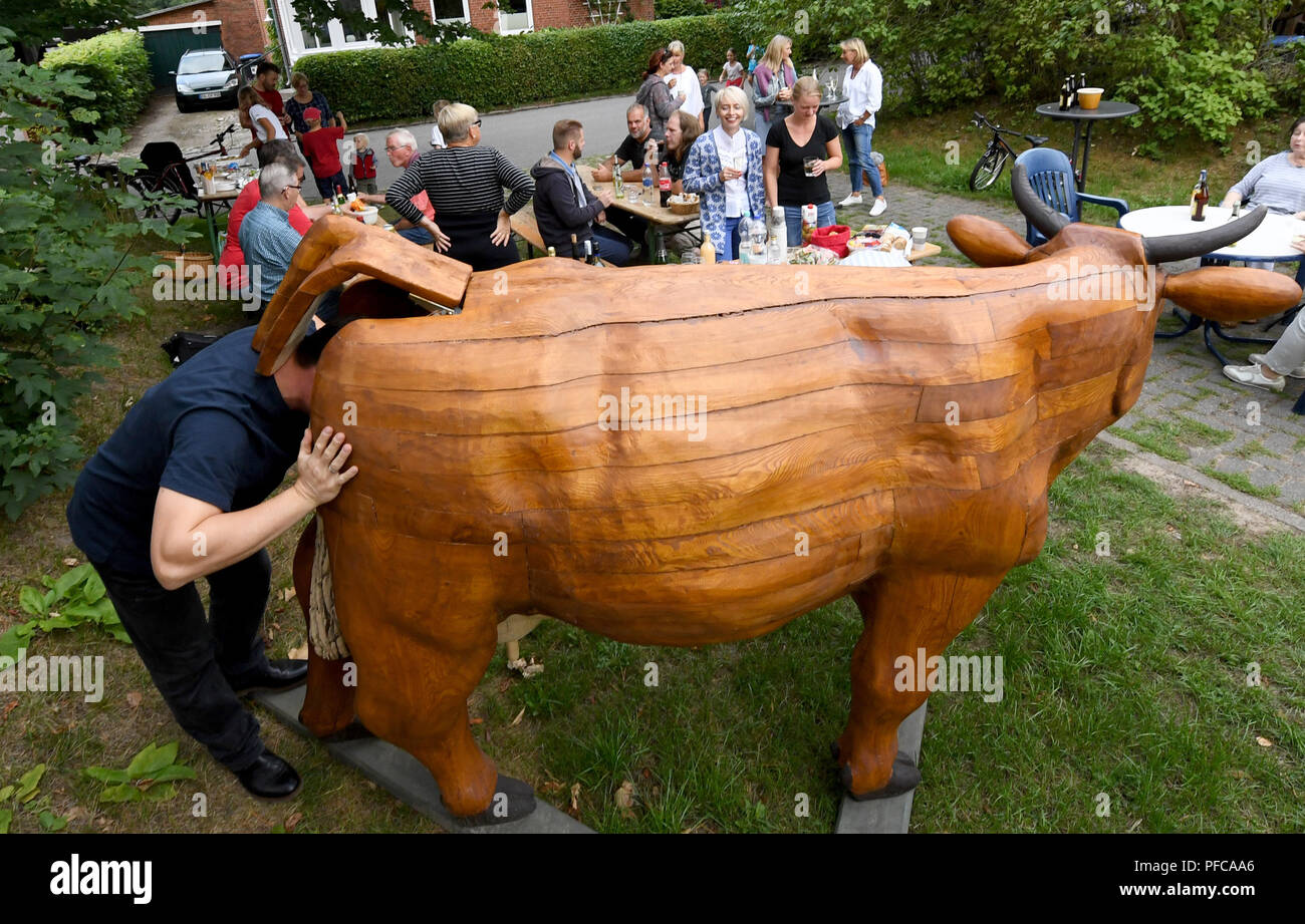 Aukrug-Homfeld, Germany. 19th Aug, 2018. A visitor of a neighbourhood meeting examines the interior of the wooden cow 'Gerda Muh'. An anonymous artist created the wooden cow, since Whitsun it has appeared in changing gardens in the district of Homfeld. With this event, the initiator wants to stimulate the discussion about agriculture and the community feeling of the villagers. Credit: Carsten Rehder/dpa/Alamy Live News Stock Photo