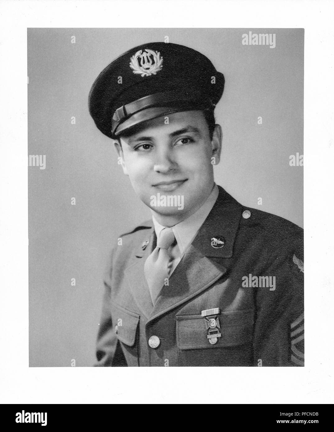 Black and white photograph, showing a formal headshot of a male soldier, looking off camera, with a very slight smile on his face, wearing a uniform with an airforce pin on the lapel, a medal, and a cap with a US Army Band insignia, likely photographed in Ohio during World War II, 1945. () Stock Photo