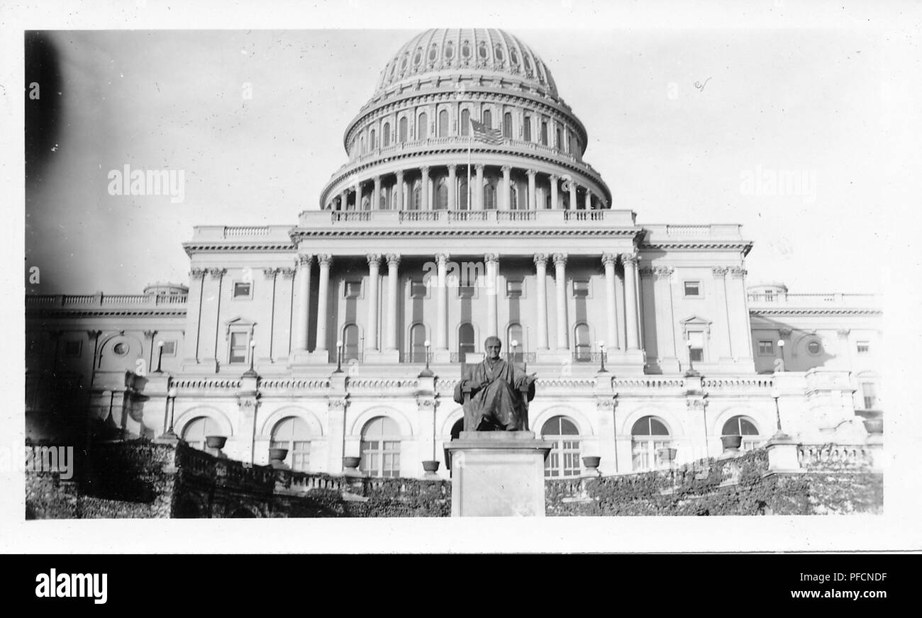Black and white photograph, shot from a low angle, showing an external view of the neoclassical, United States Capitol Building, from the western elevation or front, with a vine-covered terrace and a statue visible in the foreground, likely photographed in the decade following World War II, 1945. () Stock Photo