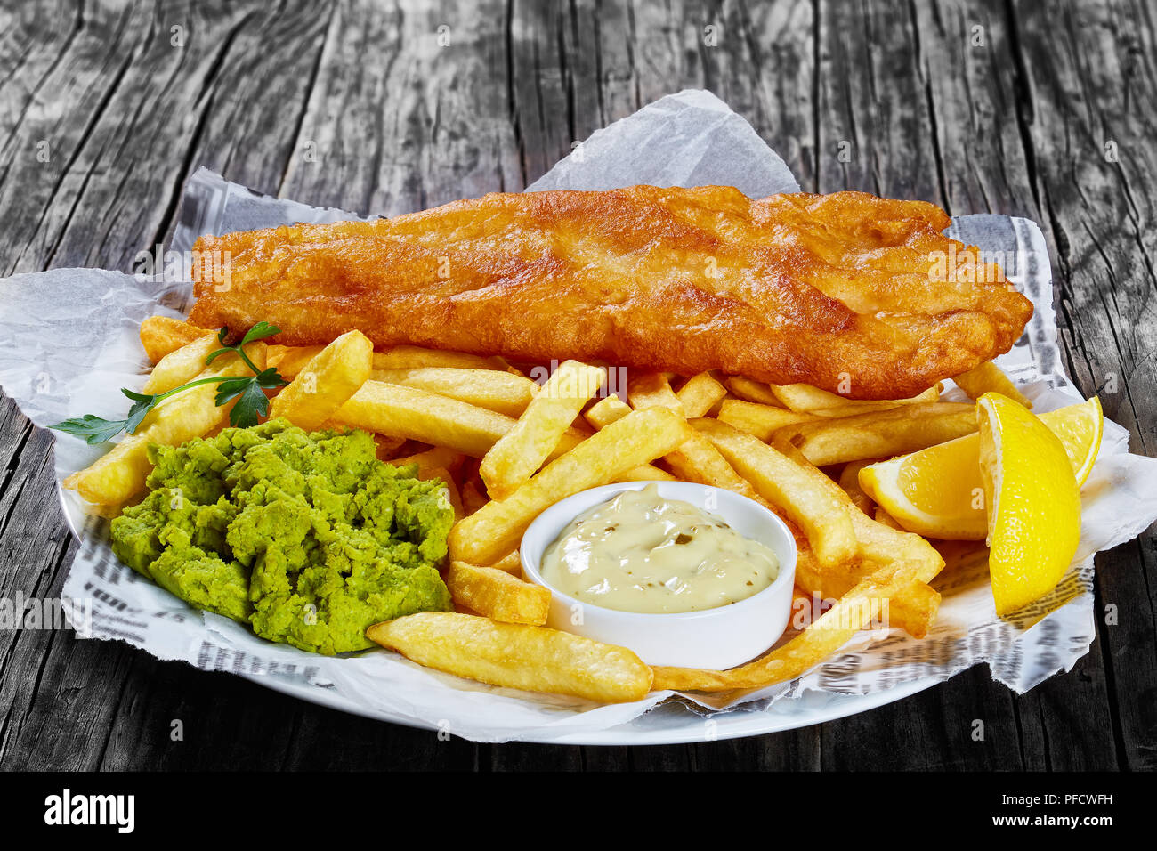 delicious crispy fish and chips - fried cod, french fries, lemon slices,  tartar sauce and mushy peas on plate on paper, on wooden table, front view  fr Stock Photo - Alamy