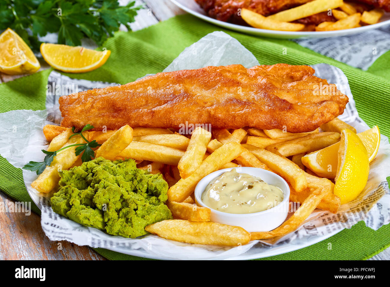 delicious crispy fish and chips - fried cod, french fries, lemon slices, tartar  sauce and mushy peas on plate on paper. parsley and lemon wedges on wo  Stock Photo - Alamy