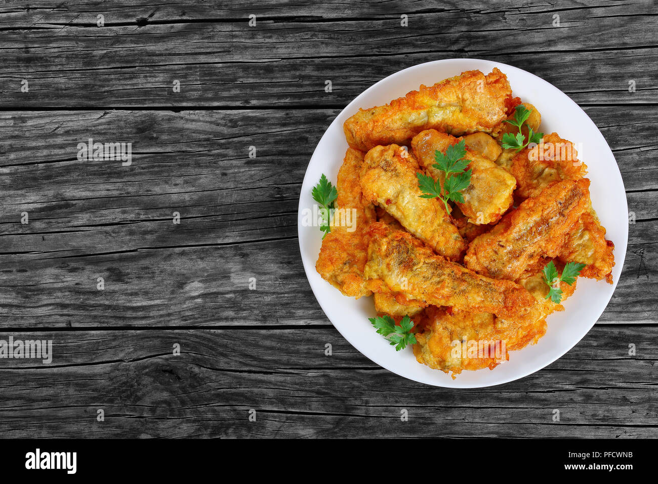 delicious golden batter deep fried fish fillets, served on white plate on old dark wooden