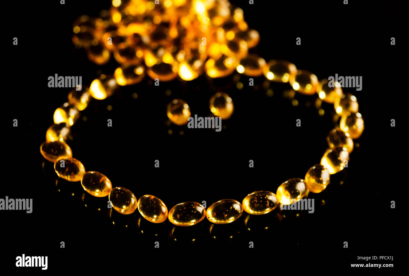 Gold necklace of fish oil capsules on black background Stock Photo