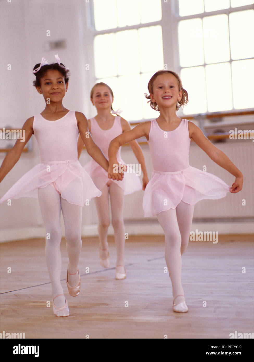 Three young ballet dancers holding skirts while running across studio