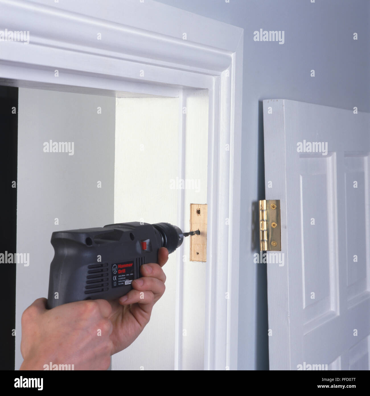 Person drilling holes into door frame with door leaning against the wall, front view Stock Photo