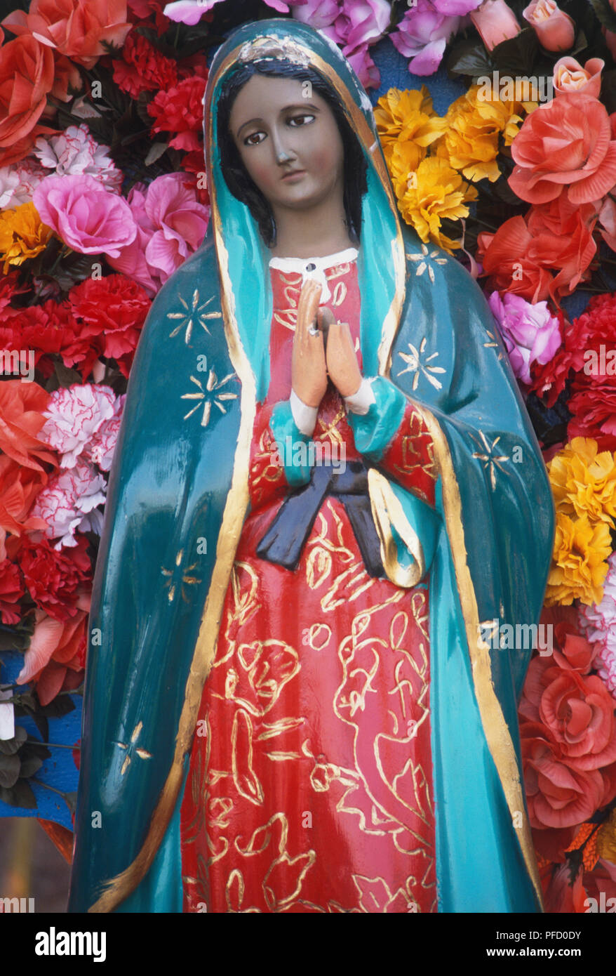 Mexico, painted statue of the Virgin of Guadalupe, patron saint of Mexico,  surrounded by colourful flowers Stock Photo - Alamy