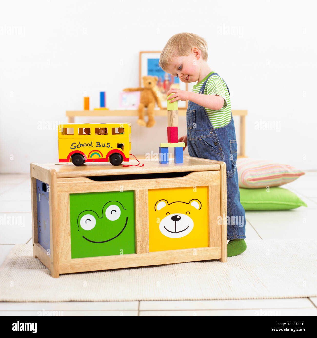 Boy playing with building blocks beside a wooden trunk with smiling faces,  double decker bus on top, shelf and teddy bear in background, blurred Stock  Photo - Alamy