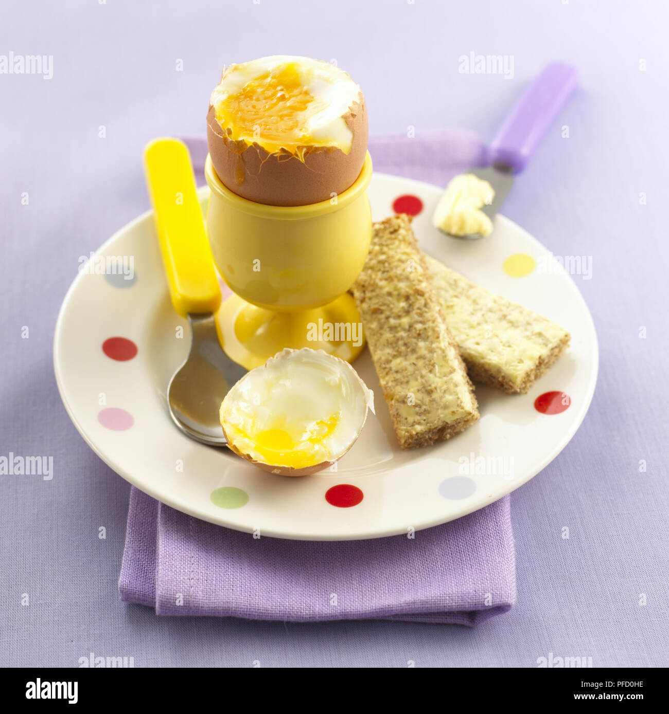 Soft-boiled egg in an egg cup, removed top, spoon and bread 'soldiers' on the side, close up. Stock Photo