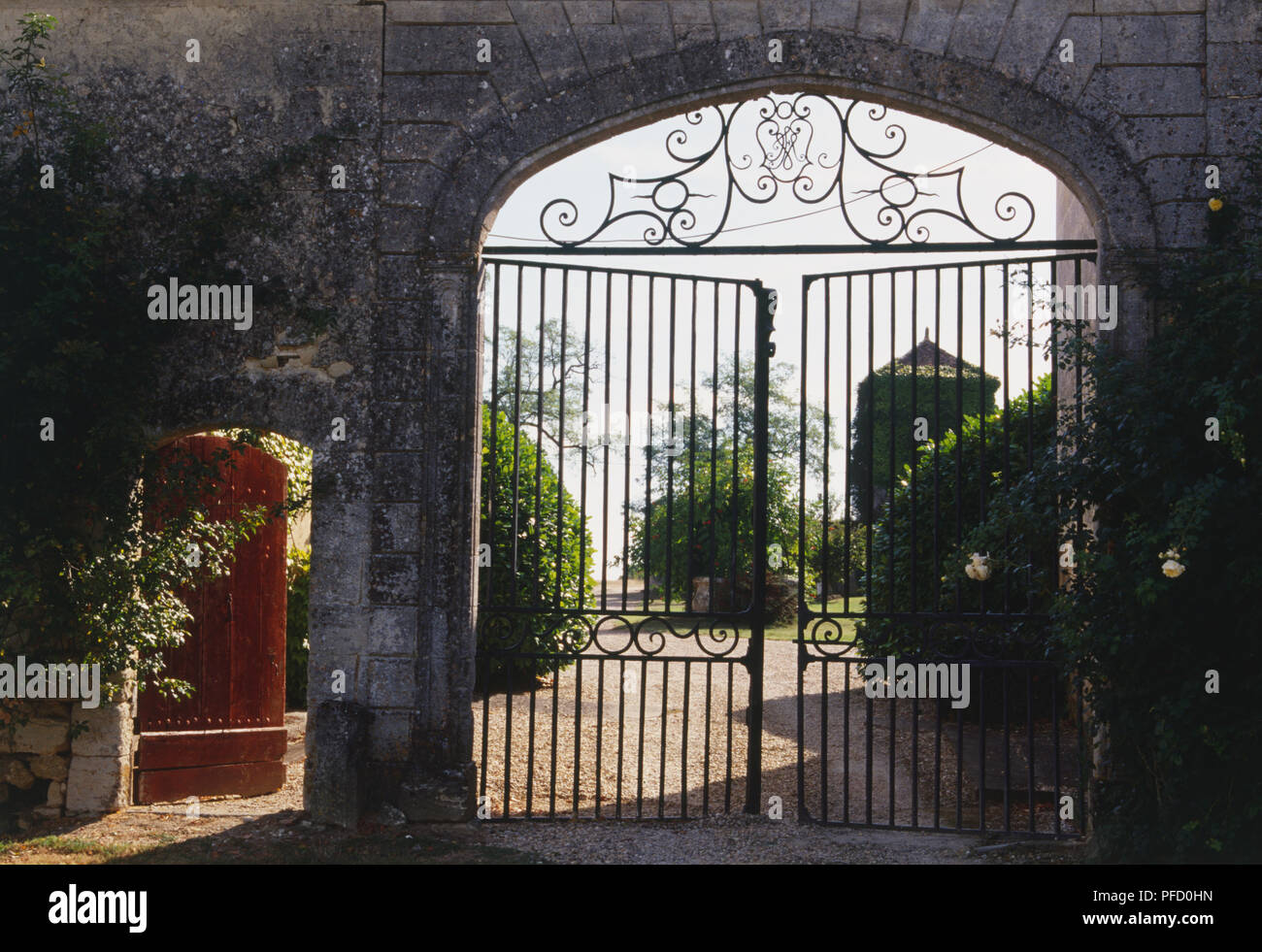 Wrought iron gates in stone archway, adjacent wooden door open to side