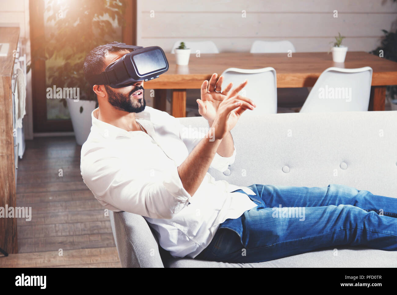 Multicultural bearded man laying on the sofa and using virtual reality goggles in the modern flat Stock Photo