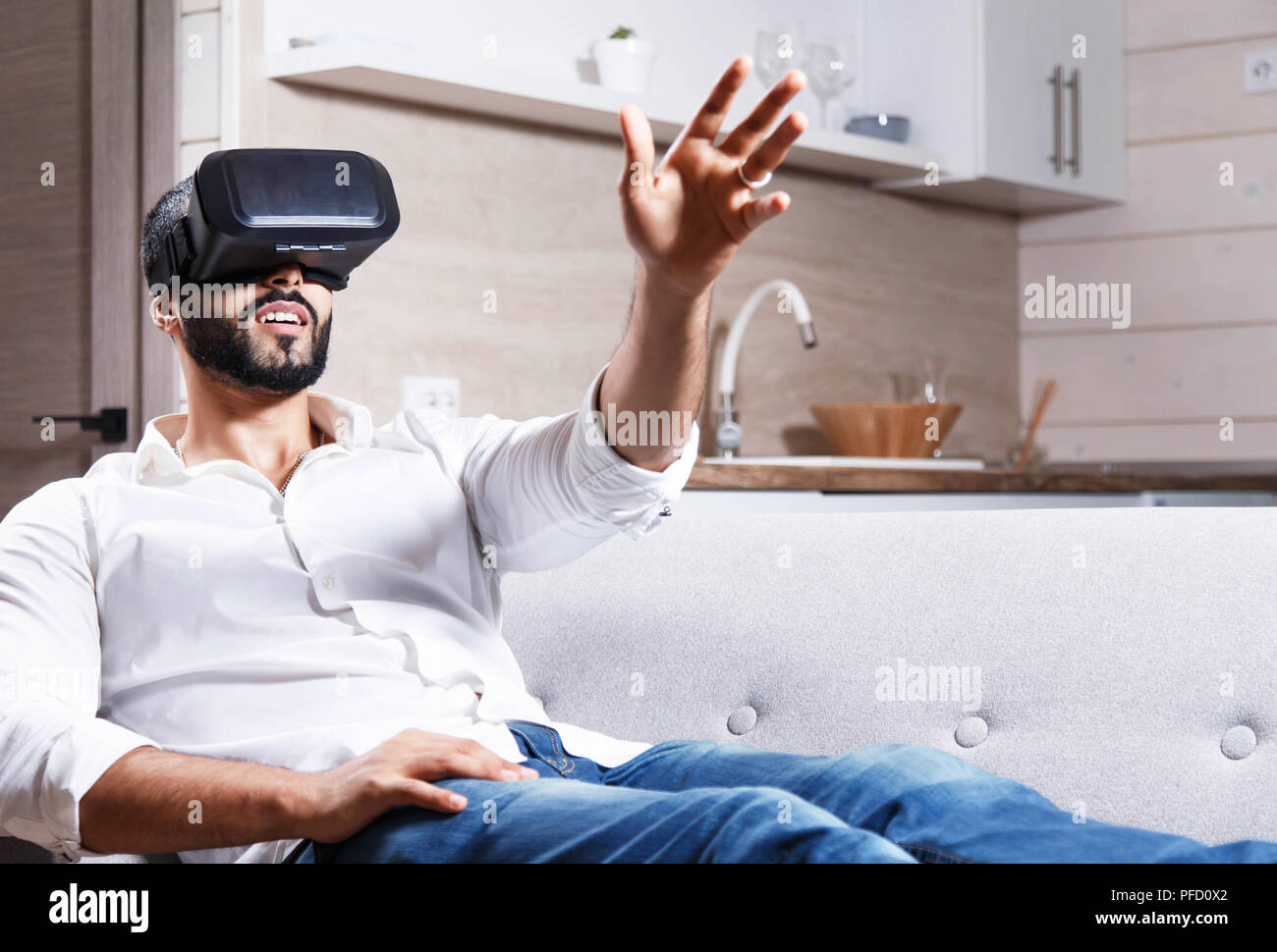 Multicultural bearded man laying on the sofa and using virtual reality goggles in the modern flat Stock Photo