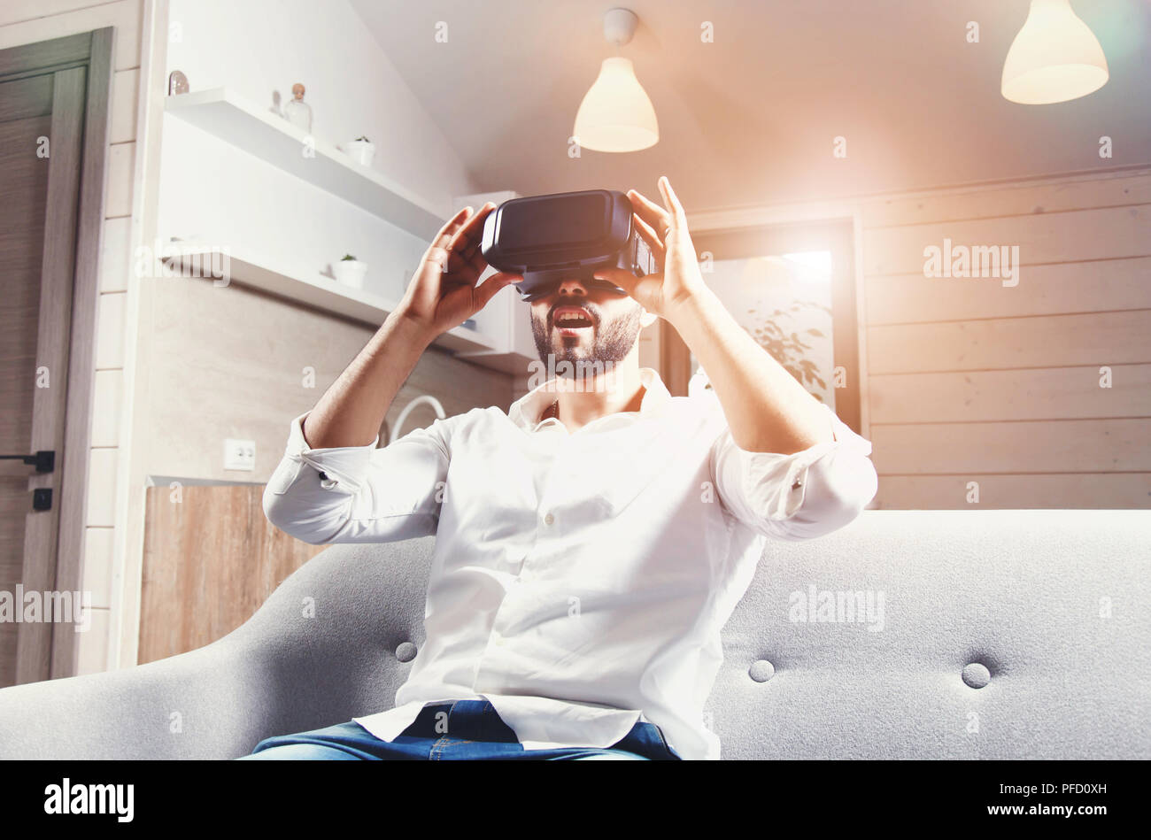 Multicultural bearded man laying on the sofa and using virtual reality goggles in the modern flat Stock Photo