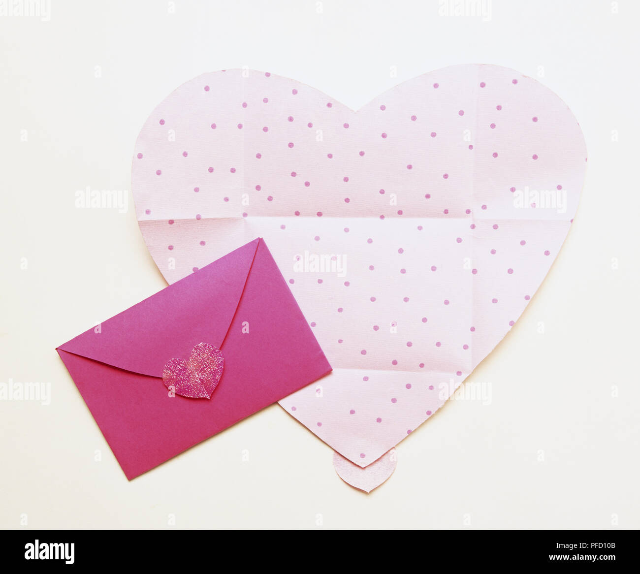 Cut out of pale pink heart with dots, and cerise envelope fastened with red cut out heart Stock Photo