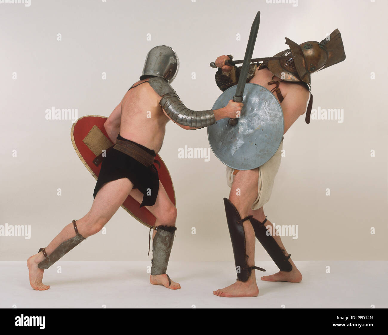 Gladiator attacking opponent with a sword, both men holding shields and wearing protective helmets, side view. Stock Photo