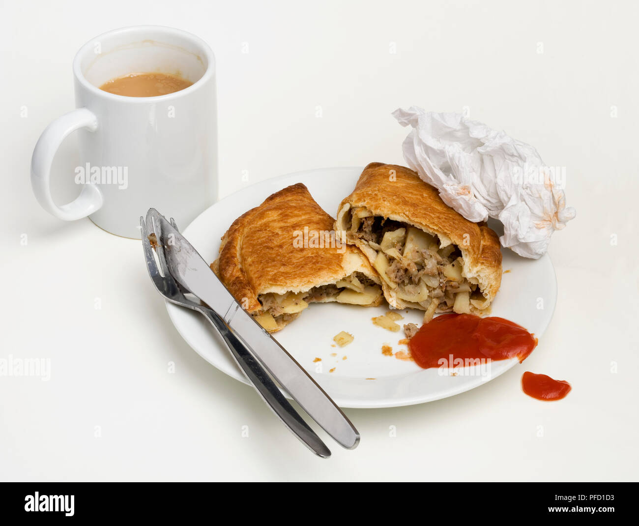 Cornish pasty, stuffed with beef, potatoes and onions, served on a plate with tomato ketchup, cutlery, crumpled napkin, mug of tea Stock Photo