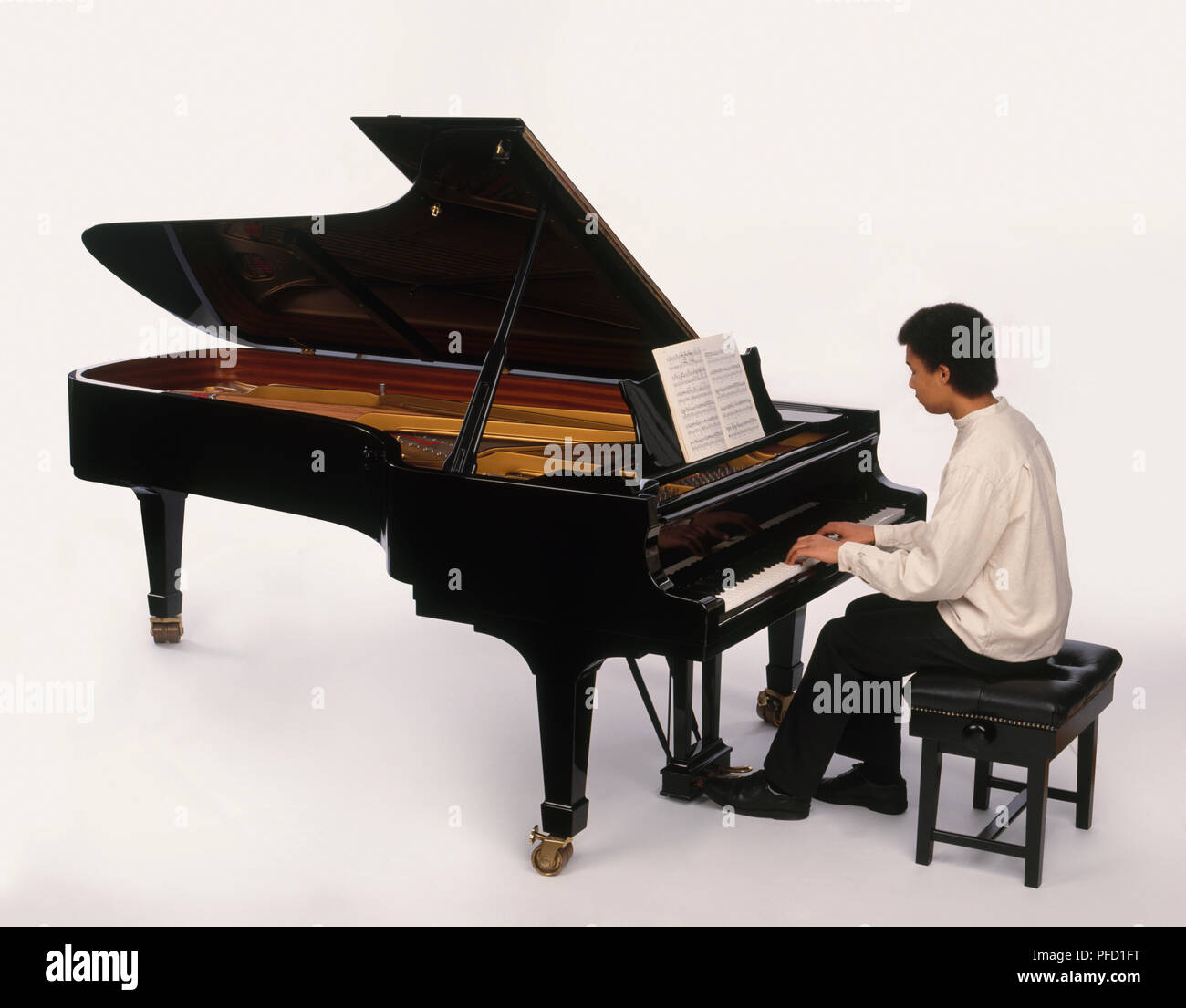 Teenage boy playing grand piano, reading from sheet music, side view Stock Photo