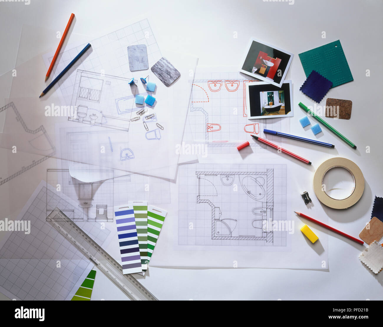 Interior design materials including floor plans on graph paper, tracing paper, colour samples, pens, pencils, pencil sharpener, ruler, photographs, tiles, masking tape and drawing tacks, view from above. Stock Photo