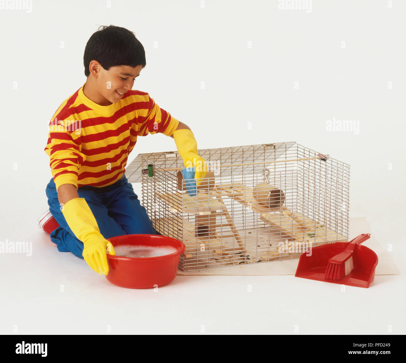 Smiling boy wearing rubber gloves kneeling by hamster cage and cleaning its bars one hand on bowl of soapy water and the other holding cloth Stock Photo Alamy