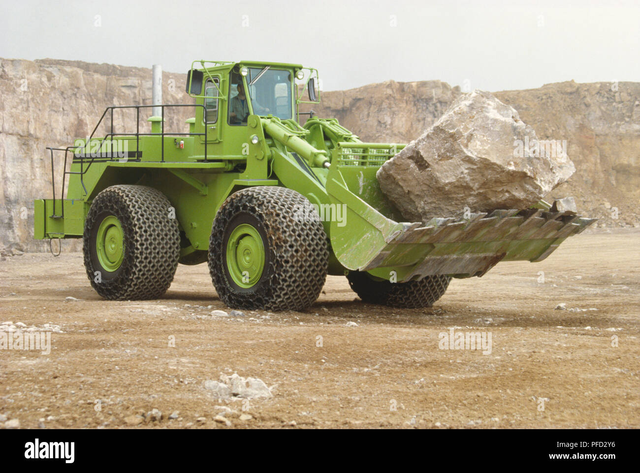 Large green loader with blade at the front carrying a heavy rock. Stock Photo