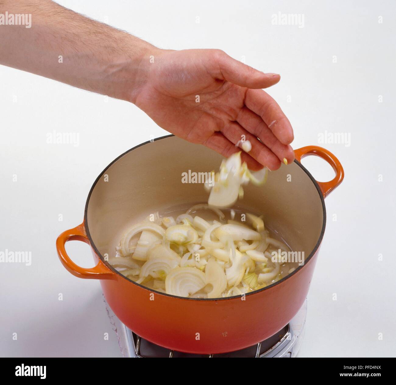 Hand adding chopped onion rings to saucepan containing oil (making a ...