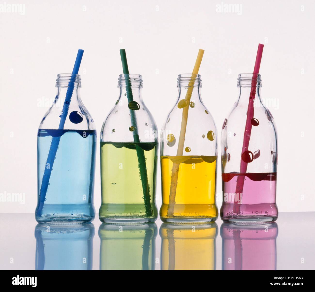 Four glass bottles containing coloured water and coloured straws (blowing into straws to create