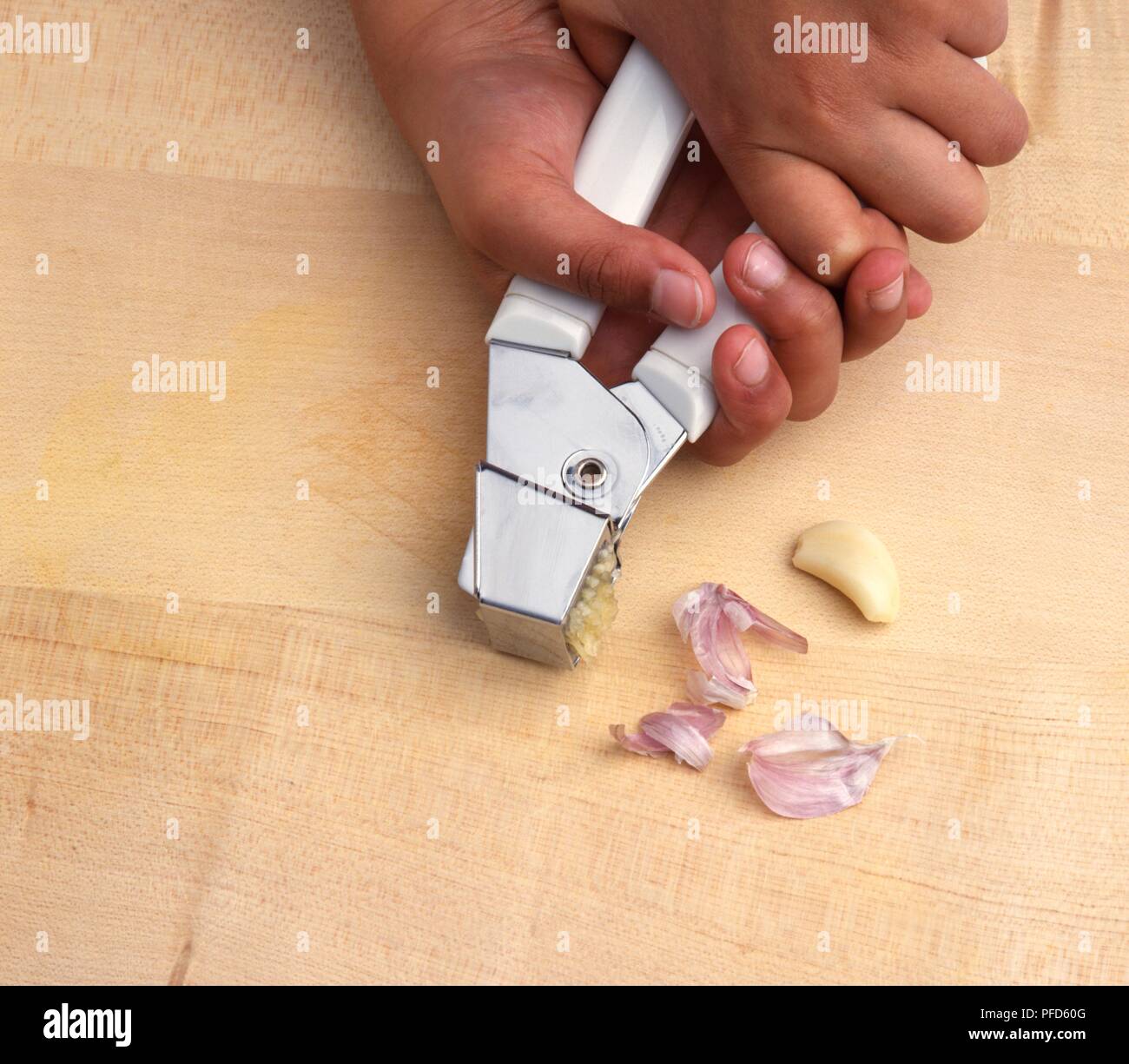 Boy's hands squeezing garlic cloves through garlic press, closeup